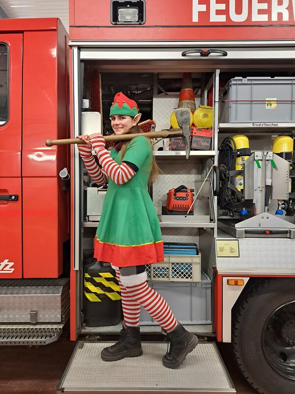 Weihnachtselfe mit Axt vor dem geöffneten Geräteraum des Löschfahrzeugs, Dezember 2024