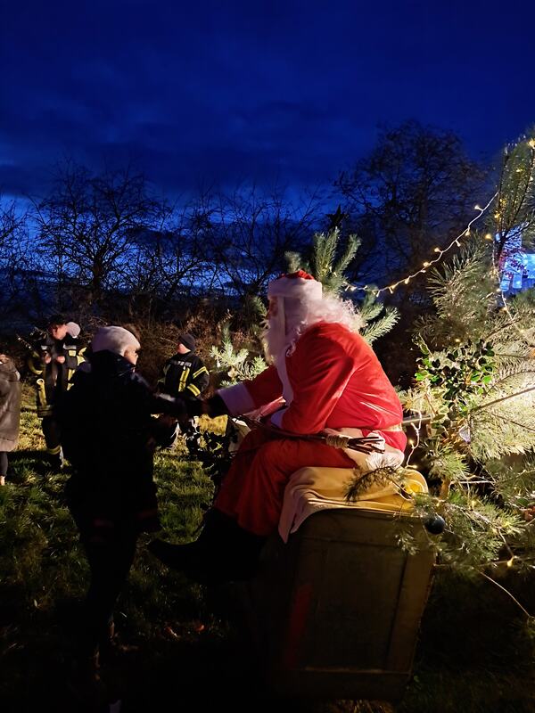 Der Weihnachtsmann sitzt am geschmückten Tannenbaum, Besucher kommen am Abend vorbei, Dezember 2025
