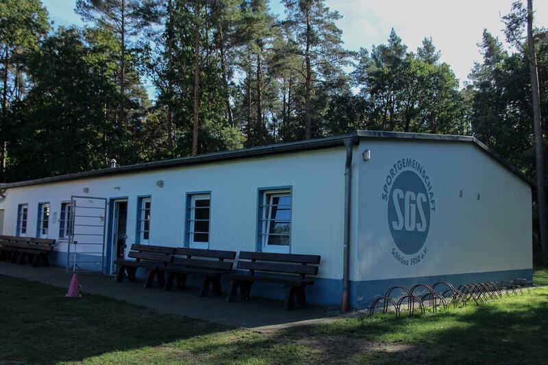 Sportlerheim von der Seite mit Vereinslogo und Bänken