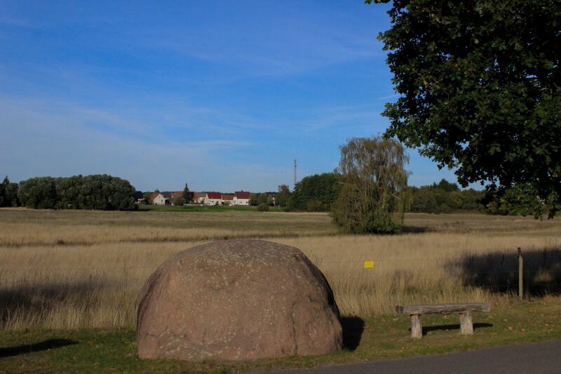Der Teufelsstein aus der Nähe, dahinter Feld und Dorfrand